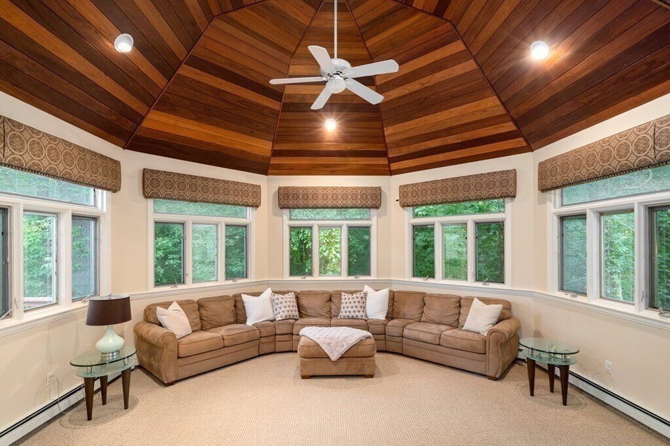 Elegant sunroom renovation with a cozy sectional sofa and natural light, part of a home addition project in Boston by Thomas Buckborough