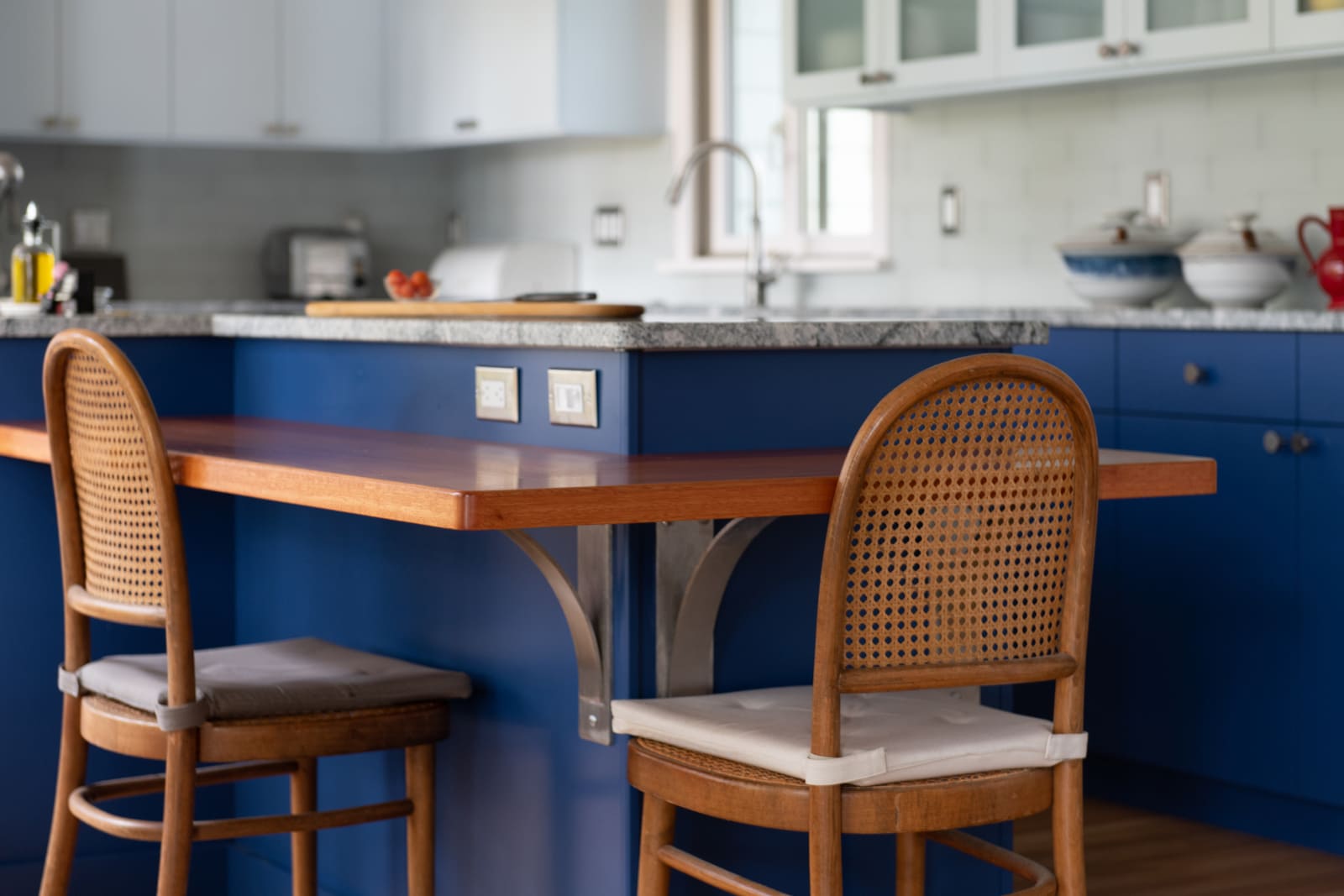 A close-up of the kitchens warm wood breakfast bar, blue cabinetry, and stylish woven chairs in Acton, MA