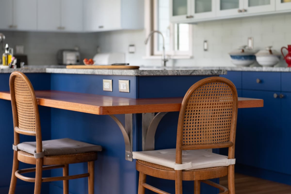 A close-up of the kitchens warm wood breakfast bar, blue cabinetry, and stylish woven chairs in Acton, MA