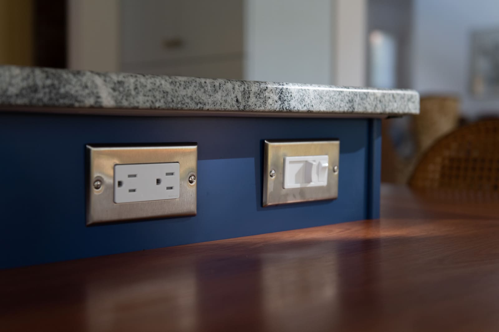 Stainless steel electrical outlets and switches embedded in a blue kitchen island with granite countertops in Acton, MA