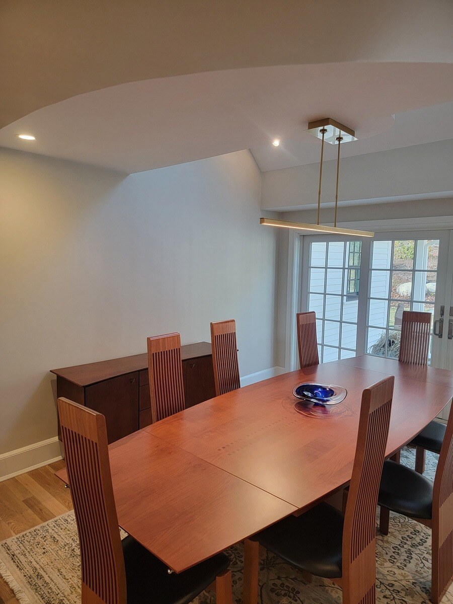 An elegant dining room with a statement pendant light and modern furnishings, featured in a home renovation by Thomas Buckborough & Associates in Acton, MA
