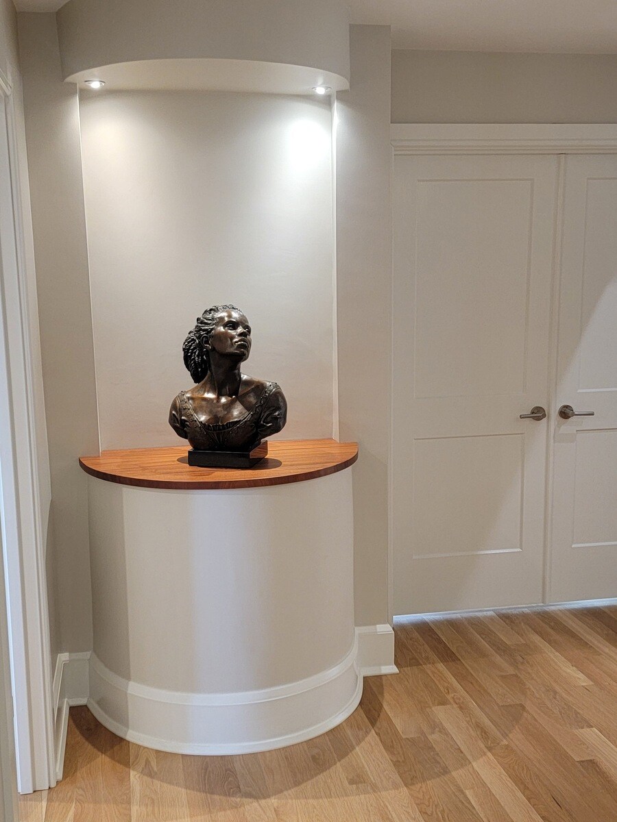 Close-up of a bronze bust displayed in a custom-built recessed niche with soft accent lighting, part of a high-end remodel in Acton, MA