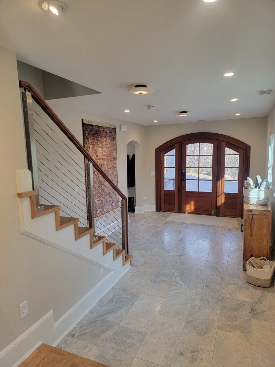 Open foyer with natural light, featuring a custom wooden staircase and sleek metal railings, part of a Frankel home remodel in Acton, MA