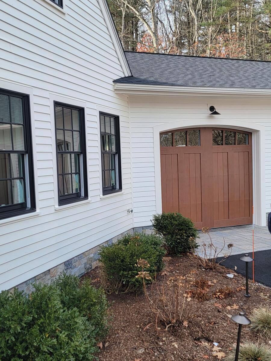 White-clad home with black windows and an arched wooden garage door, part of the Frankel remodel in Acton, MA