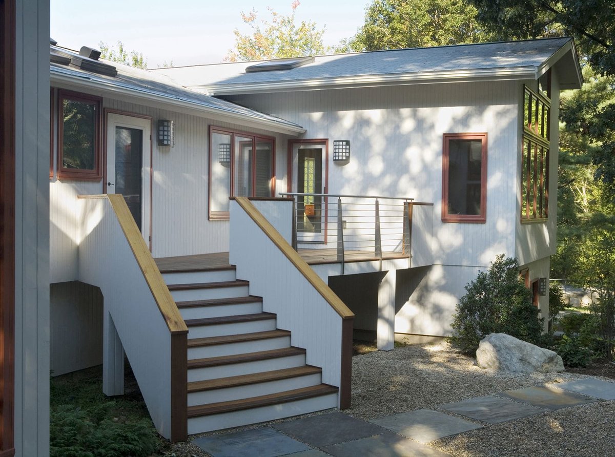 Rear exterior of a modern home featuring a cable railing system and wooden staircase, designed by Thomas Buckborough & Associates in Acton, MA