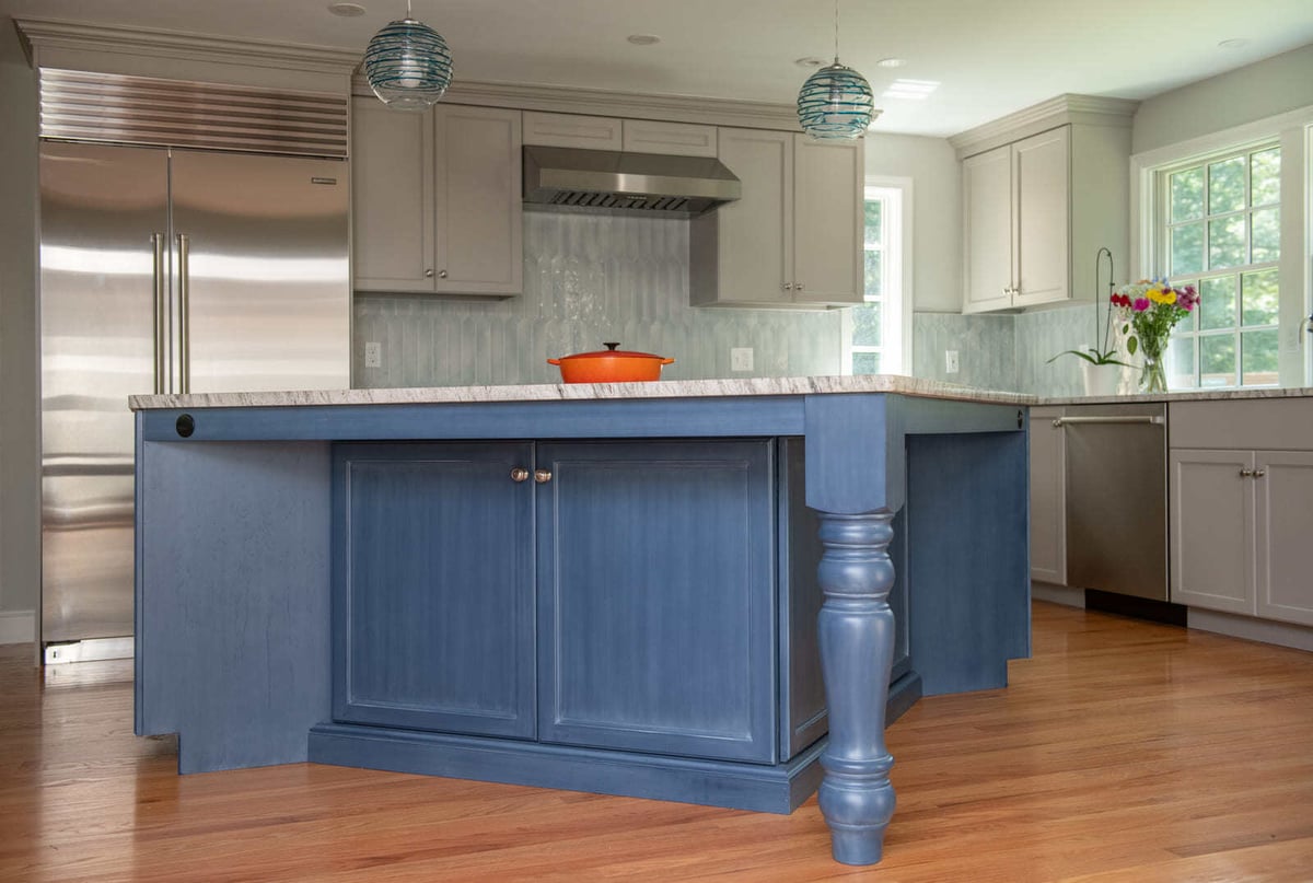 A bold blue kitchen island with turned wood legs and marble countertops in a home remodel by Thomas Buckborough & Associates