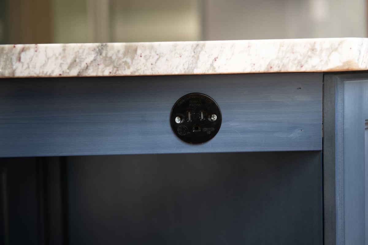 A close-up of a built-in power outlet on a blue kitchen island in a home remodel by Thomas Buckborough & Associates