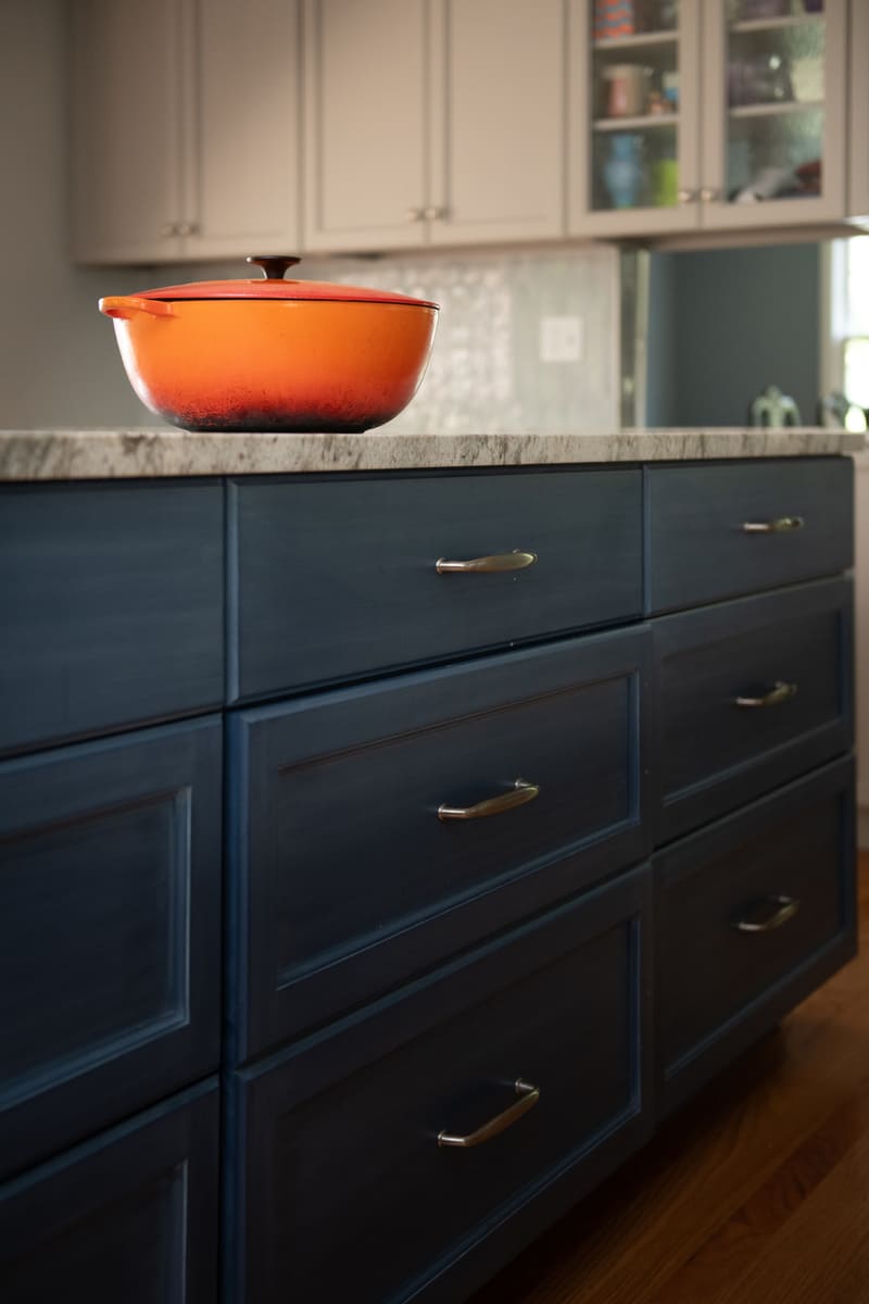 A deep blue kitchen island with a vibrant orange pot, adding character to a home renovation by Thomas Buckborough & Associates