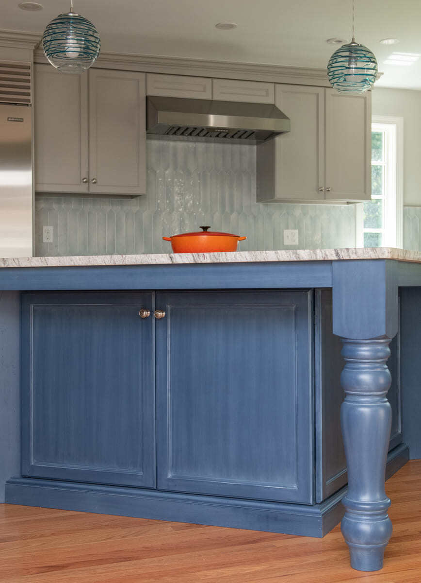 A kitchen remodel in Acton, MA, showcasing a deep blue island, quartz countertops, and a tile backsplash