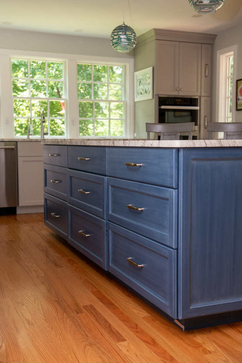 A modern kitchen island in Acton, MA, featuring deep blue cabinetry, brass handles, and marble countertops by Thomas Buckborough & Associates