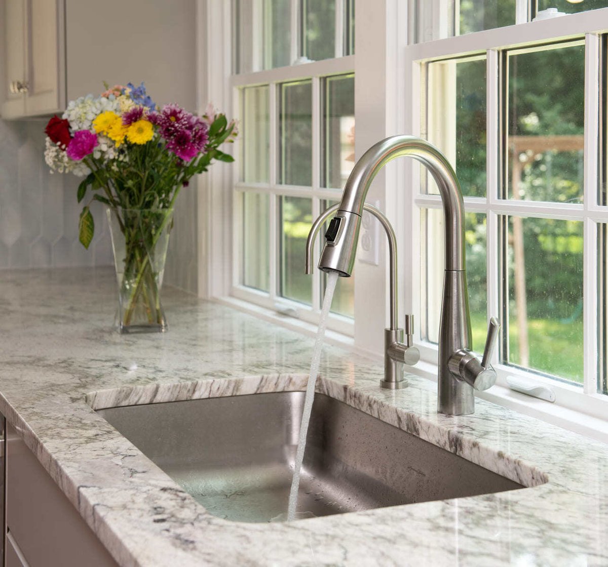 A modern kitchen sink with a stainless steel high-arch faucet and marble countertops in a home remodel by Thomas Buckborough & Associates