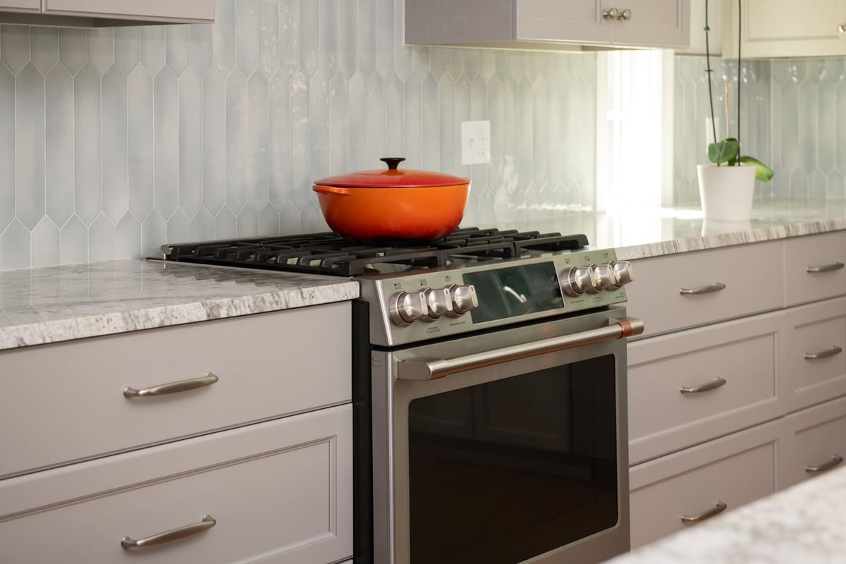 A stainless steel gas range with an orange pot, set against a sleek tile backsplash in a remodeled kitchen in Acton, MA