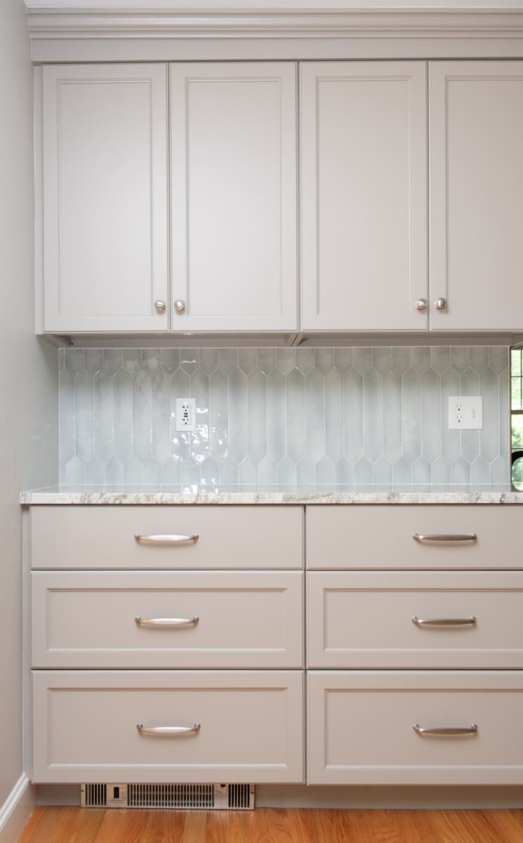 Soft gray cabinets with silver hardware complement the elegant tile backsplash in this kitchen remodel