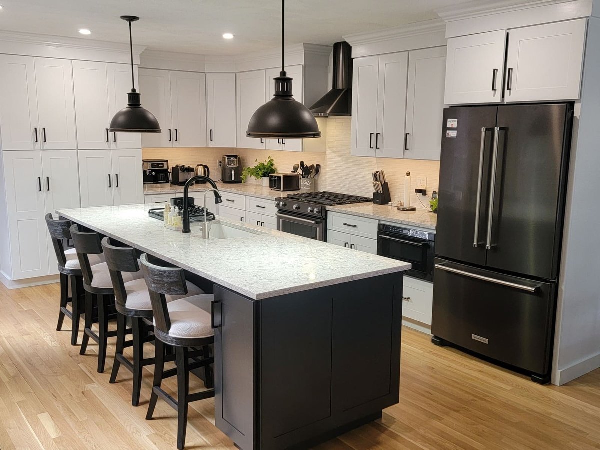 Contemporary kitchen design with a quartz countertop island, black and white cabinetry, and stainless steel appliances in an Acton, MA remodel