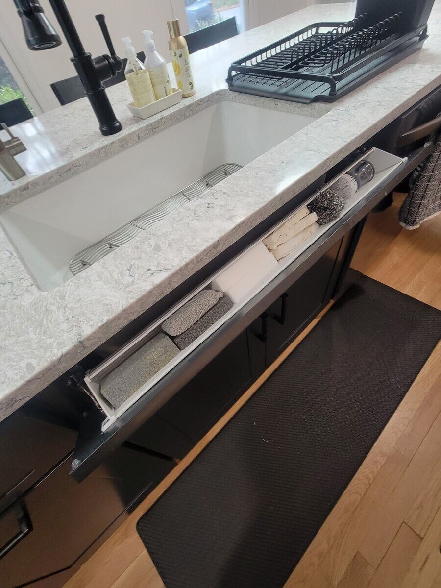 Hidden kitchen sink storage with a tilt-out tray for sponges and cleaning supplies in an Acton, MA remodel