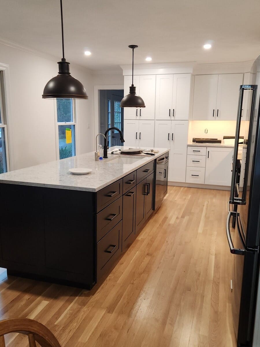Modern farmhouse-style kitchen featuring a large island, black pendant lights, and white cabinetry in an Acton, MA remodel