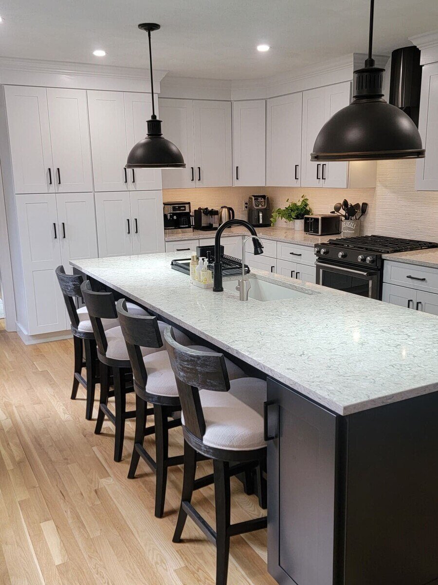 Modern white kitchen with a large island, black pendant lights, and sleek cabinetry in a Sasot Rendo Remodel by Thomas Buckborough & Associates in Acton, MA
