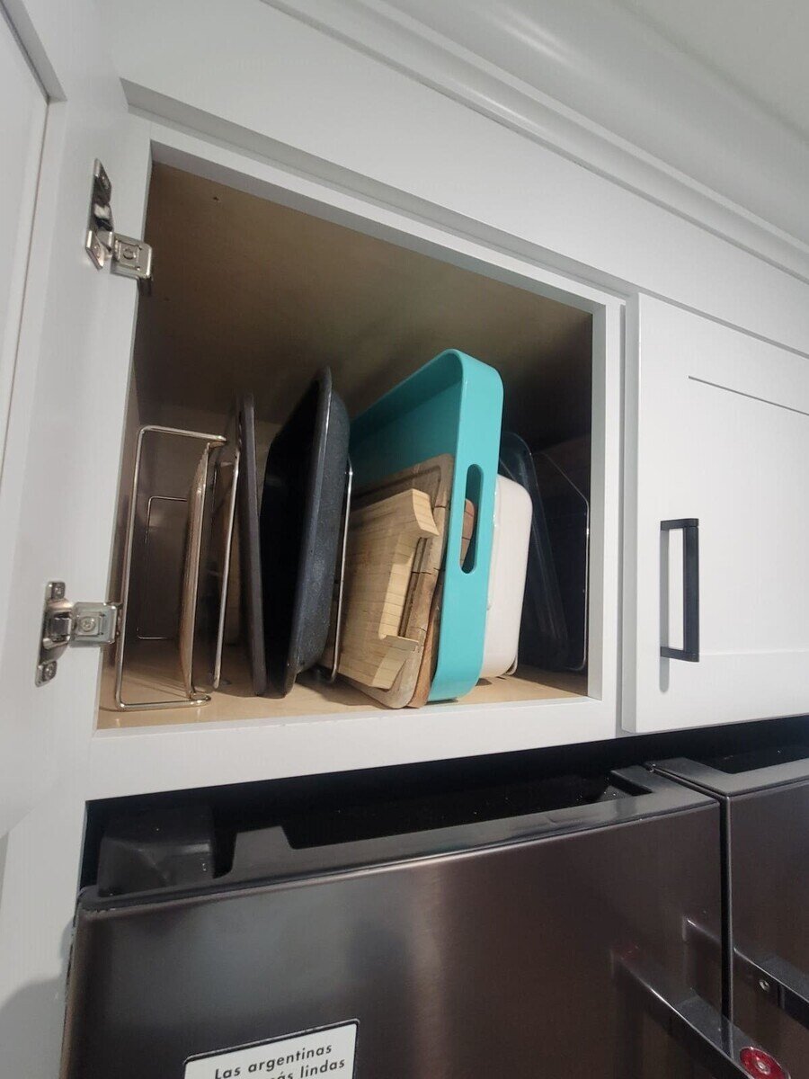 Over-the-fridge storage cabinet neatly arranged with cutting boards and baking trays in an Acton, MA remodel