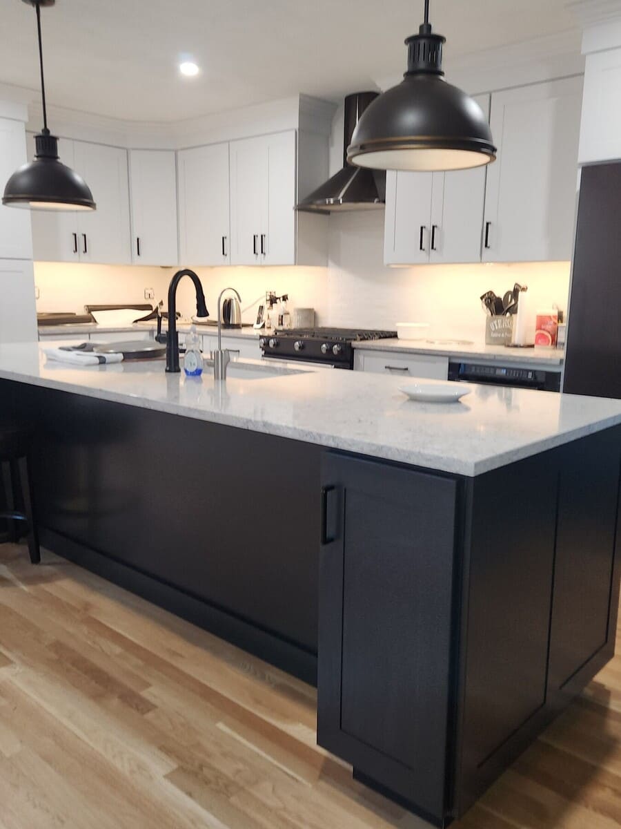 Spacious kitchen with a large black island, quartz countertops, and industrial-style pendant lights in an Acton, MA remodel