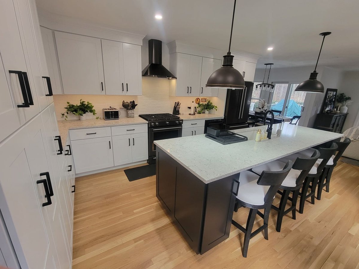 Wide-angle view of a luxury kitchen remodel featuring a quartz island, black pendant lights, and white cabinetry in Acton, MA