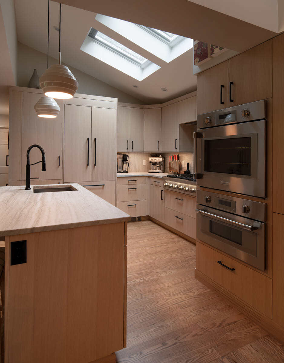 Elegant kitchen with light wood cabinets, black fixtures, and natural light from overhead skylights in Acton, MA