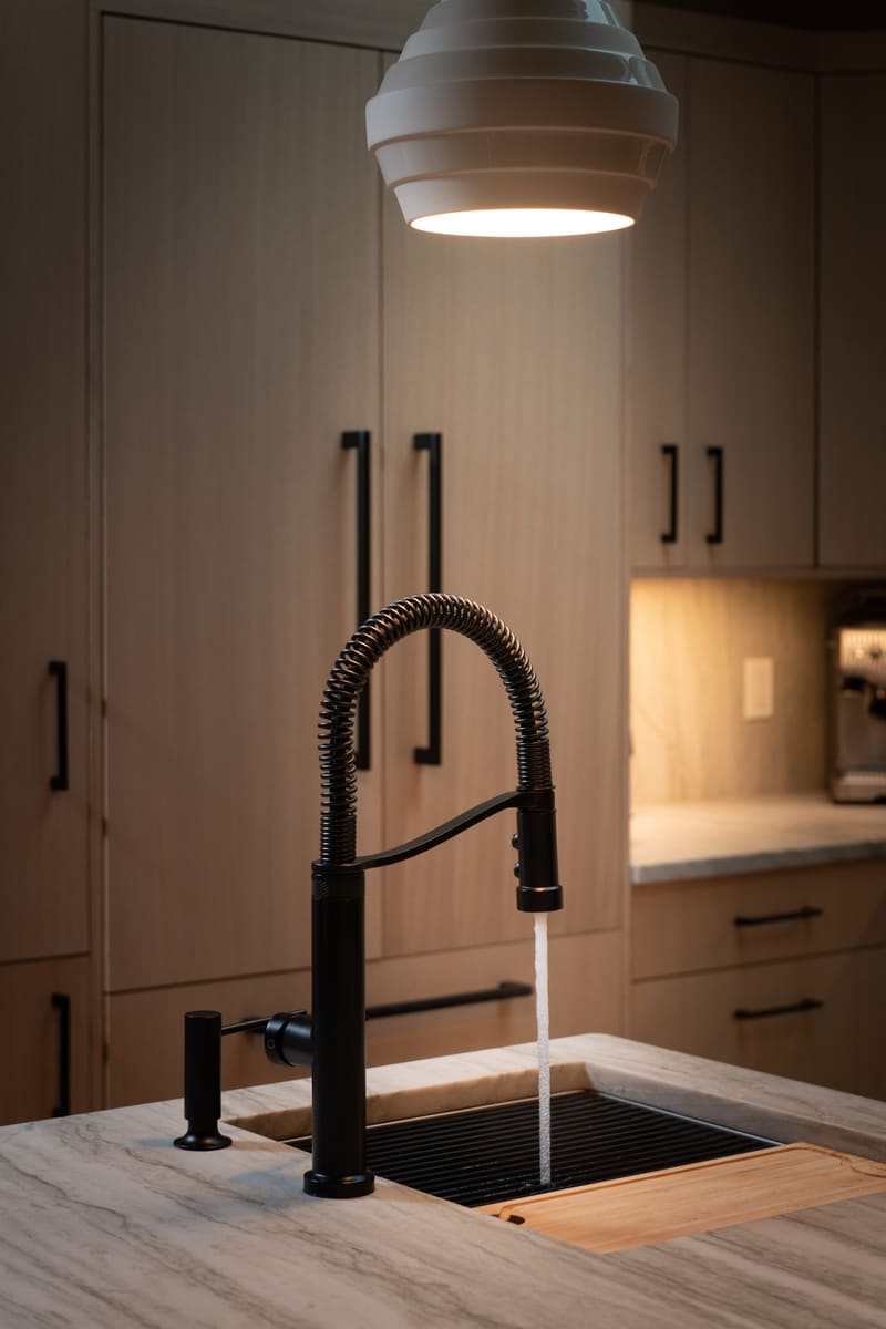 Stylish black coil spring kitchen faucet under pendant lighting in a Shea home remodel by Thomas Buckborough & Associates in Acton, MA