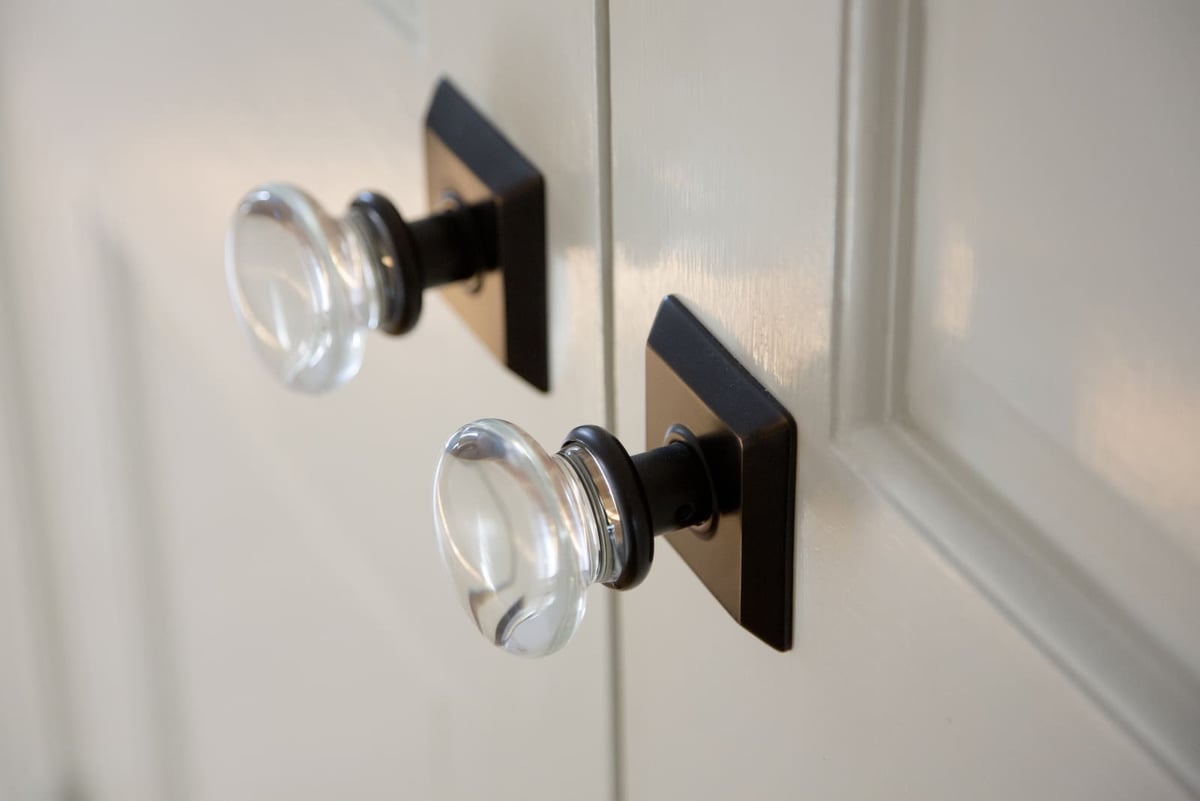 Elegant glass door knobs with black square backplates on a classic white door in a remodel by Thomas Buckborough & Associates, Acton, MA