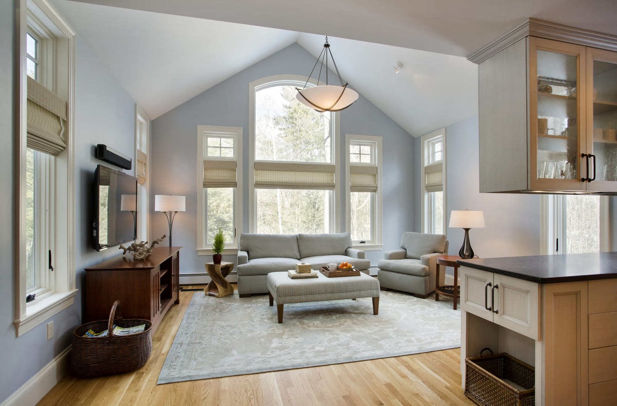Open-concept living space with high ceilings, soft blue walls, and a cozy seating area in a Massachusetts home remodel
