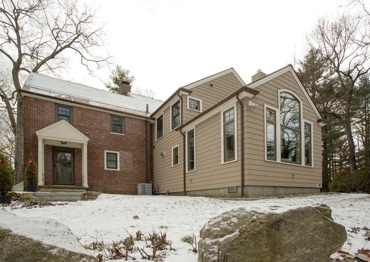 Rear view of a colonial-style home with a modern two-story addition featuring large windows, designed by Thomas Buckborough & Associates, Acton, MA