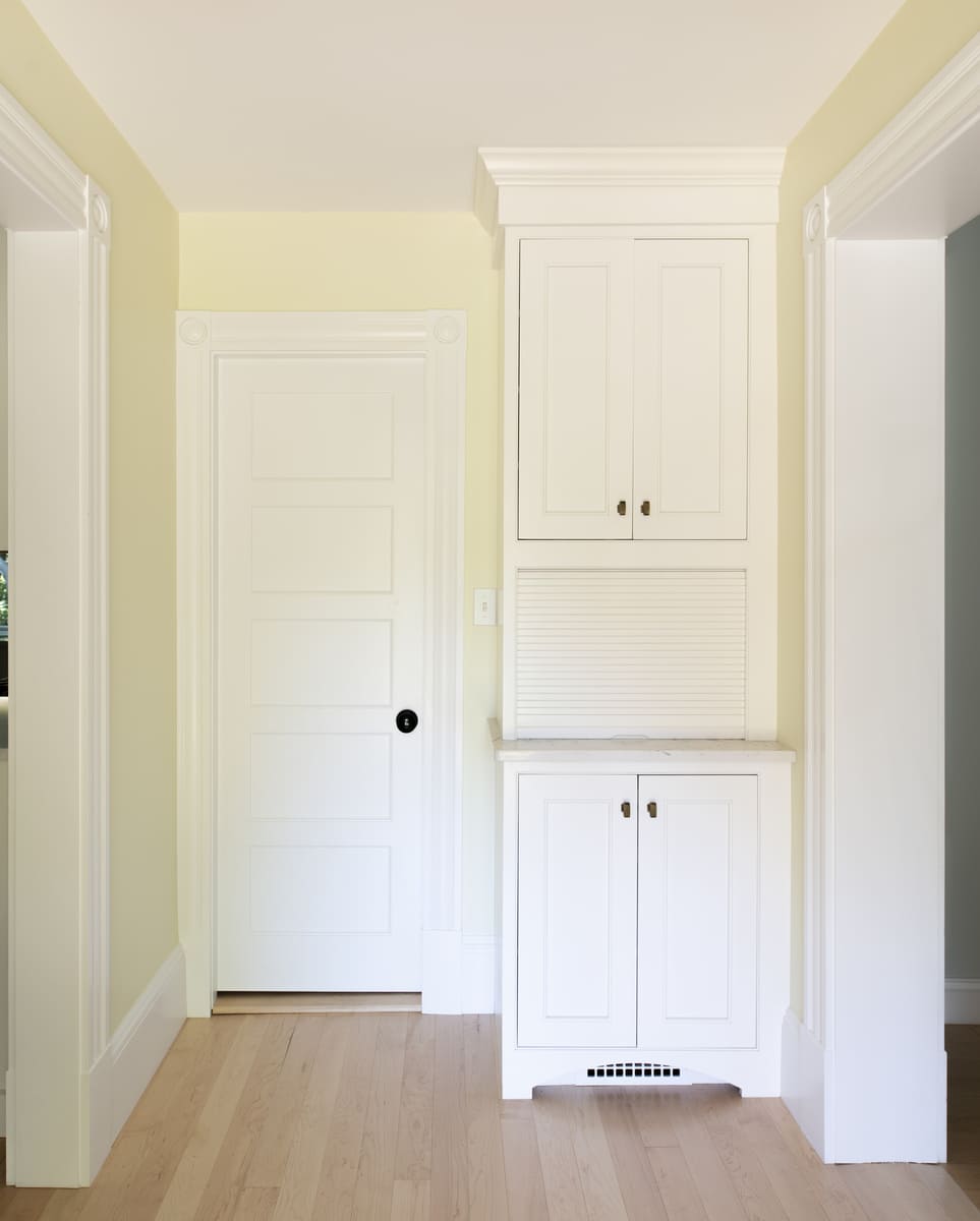 A cozy and functional home passageway with light yellow walls and white trim detailing in a New England-inspired renovation