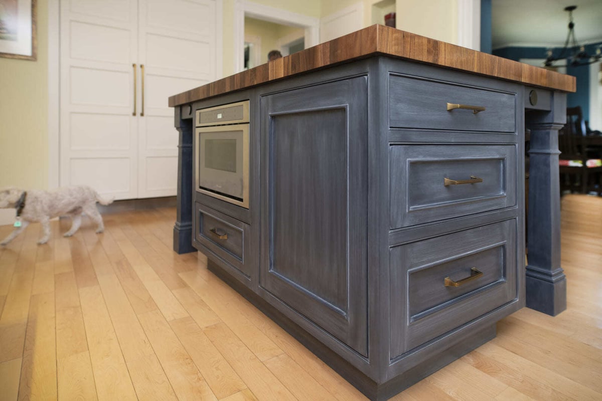 Close-up of a stunning navy blue kitchen island with brass hardware and a built-in microwave in a Tucker Remodel by Thomas Buckborough & Associates