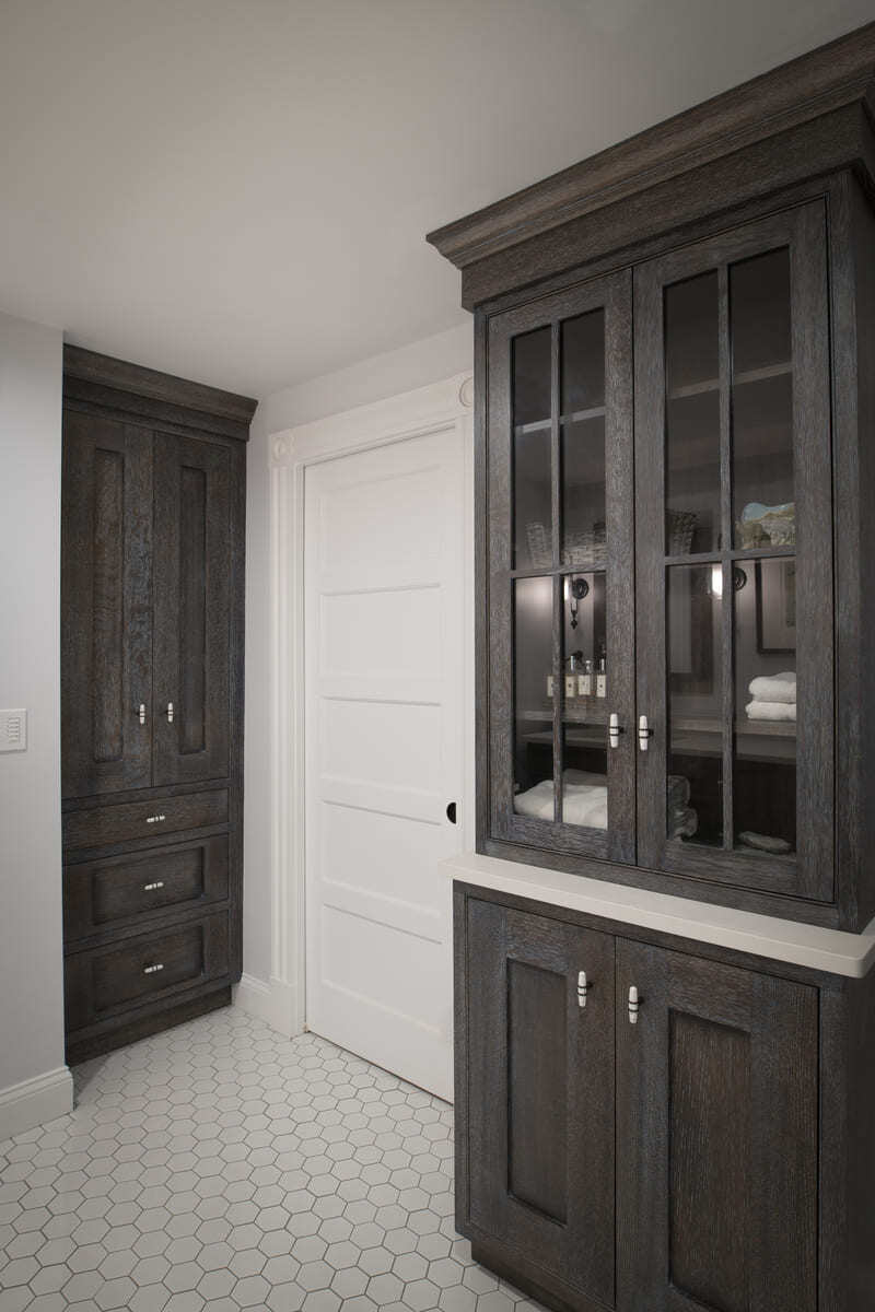 Elegant bathroom cabinetry with glass panel doors, dark wood finishes, and ample storage space in an Acton, MA home remodel