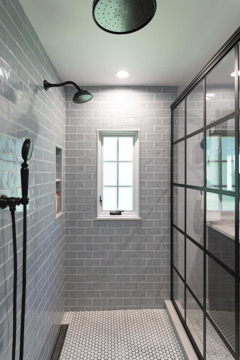 Elegant walk-in shower with a rainfall showerhead, gray subway tile walls, and a frameless glass divider in a Tucker Remodel project