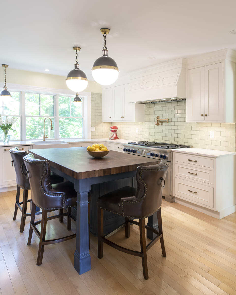 Renovated kitchen in Acton, MA featuring a navy blue island, white cabinetry, and industrial pendant lighting by Thomas Buckborough & Associates