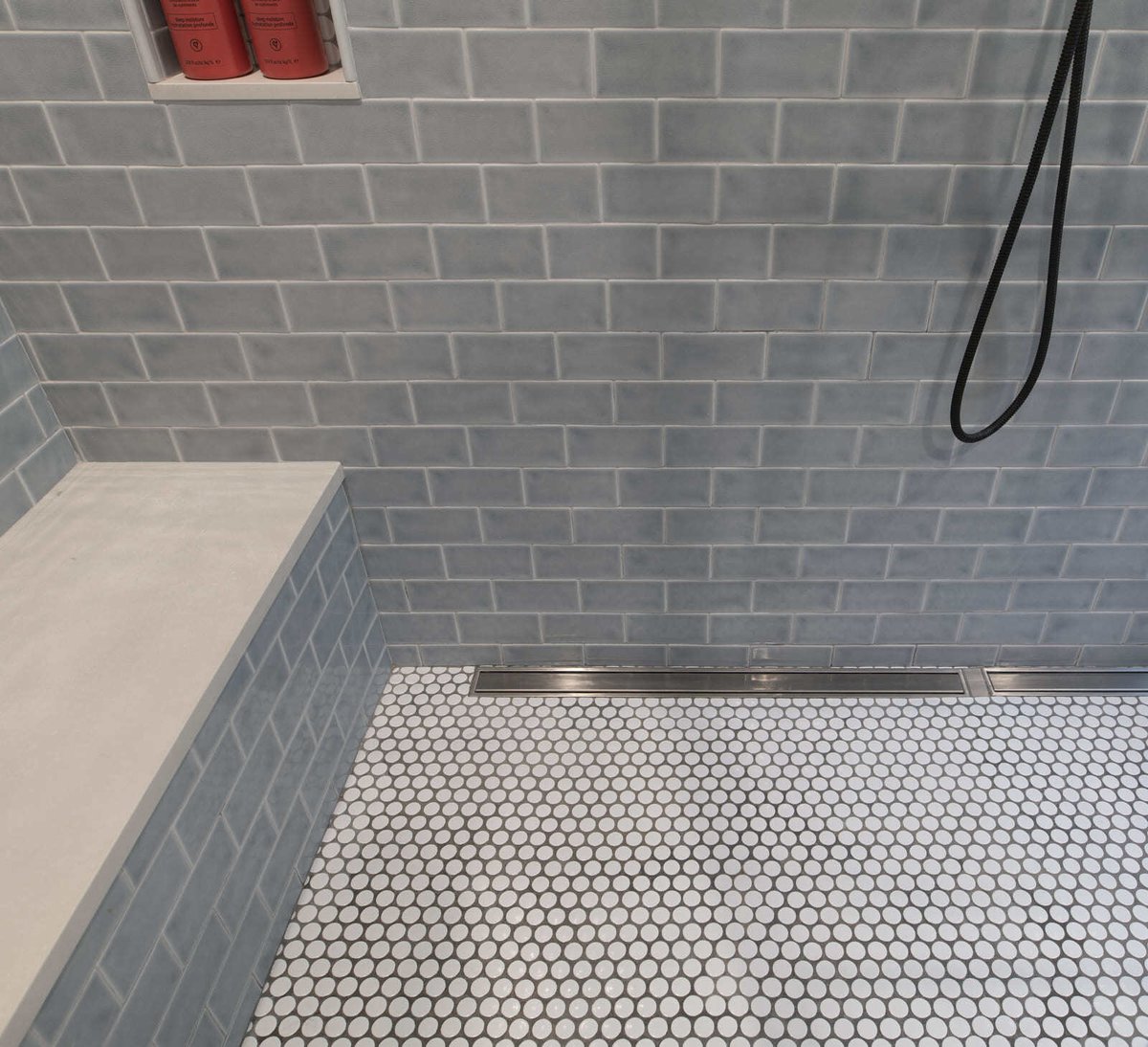 Walk-in shower featuring soft gray subway tiles, built-in storage niches, and a sleek black hand shower in an Acton, MA remodel