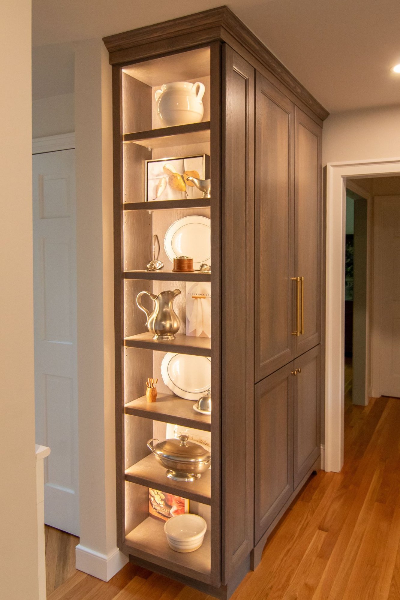 Glass-front cabinet with stacked neutral dishware above a white quartz counter and small potted plants. (3)