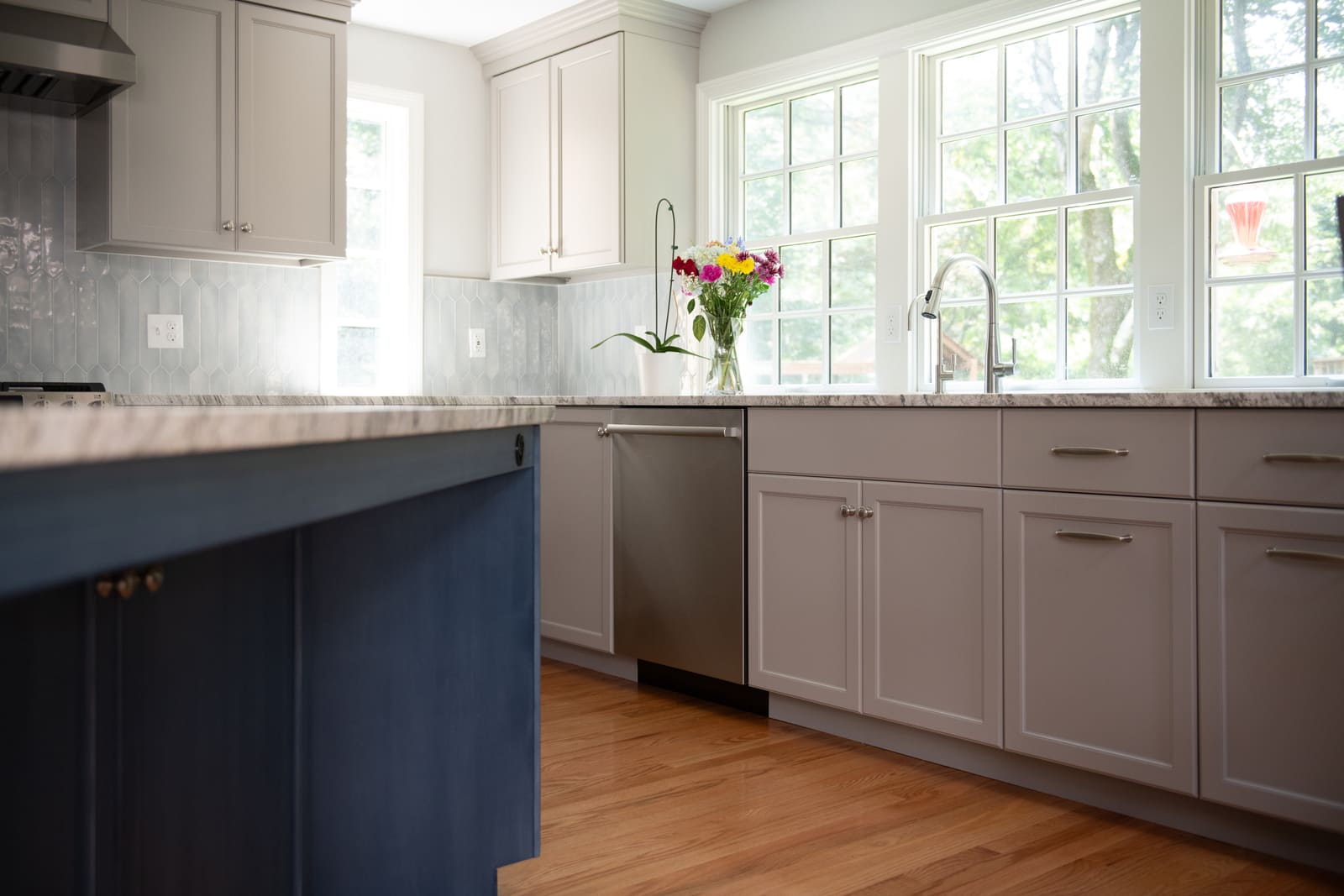 A beautifully remodeled kitchen in Acton, MA, featuring soft gray cabinetry, a marble countertop, and fresh flowers by the window