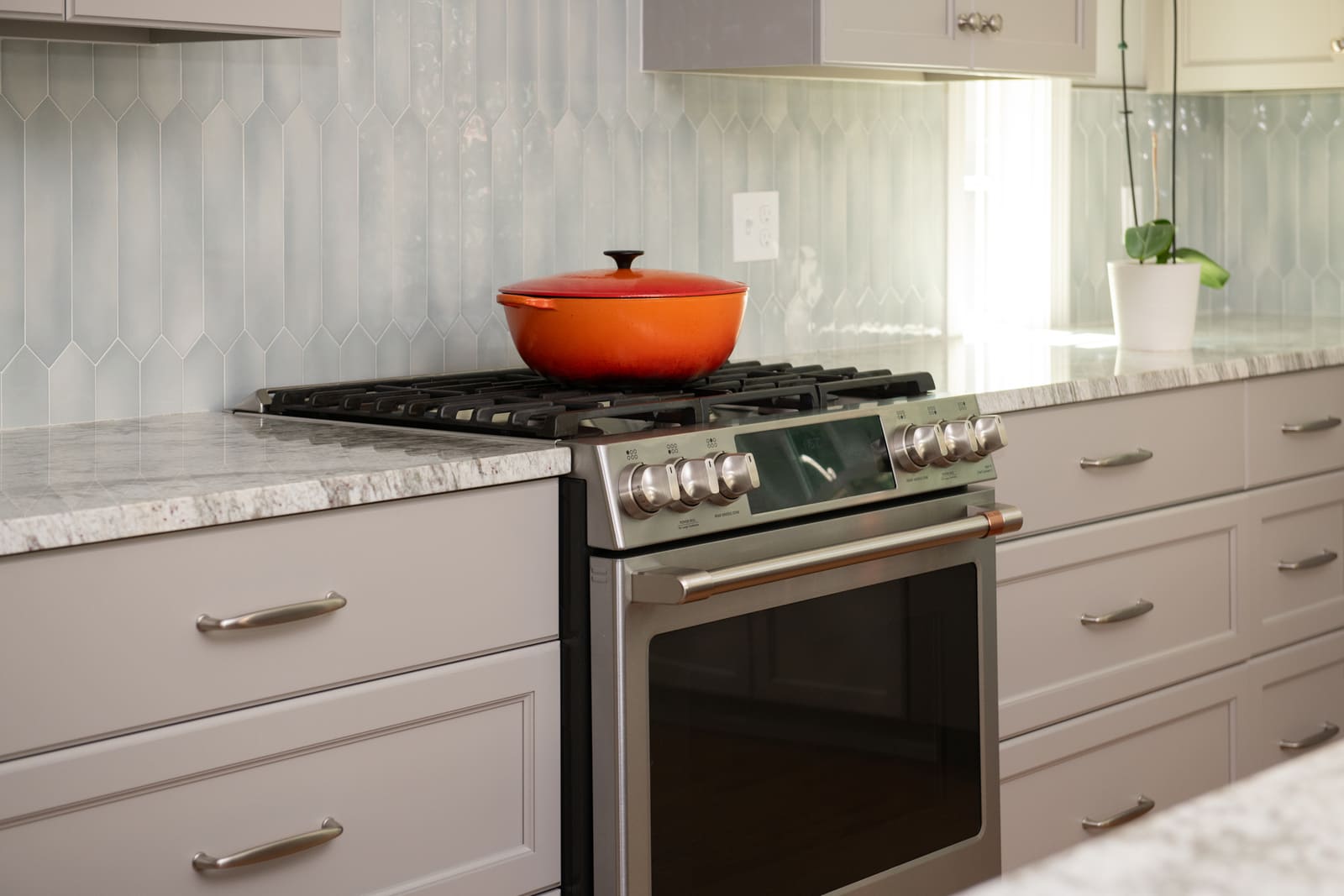 A stainless steel gas range with an orange pot, set against a sleek tile backsplash in a remodeled kitchen in Acton, MA